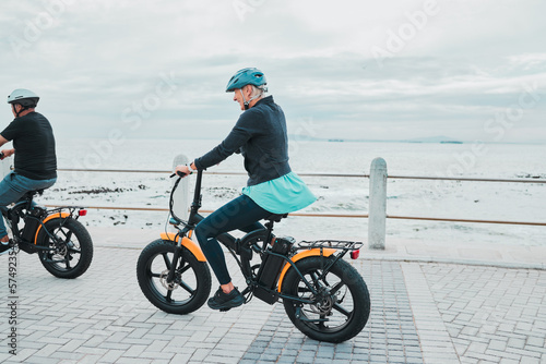 Couple, helmet or electrical bike by beach, ocean or sea in future transport, clean energy or sustainability travel. Technology, electric or eco friendly bicycle for happy woman or mature cycling man