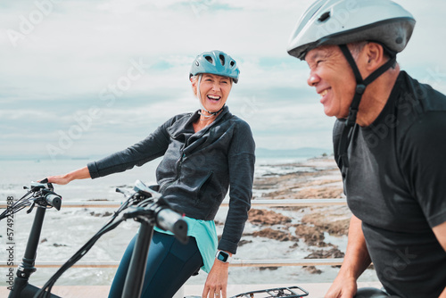 Laughing couple, helmet or electrical bike by sea in transportation, clean energy or sustainability travel bonding. Technology, electric or eco friendly bicycle for funny woman or mature cycling man