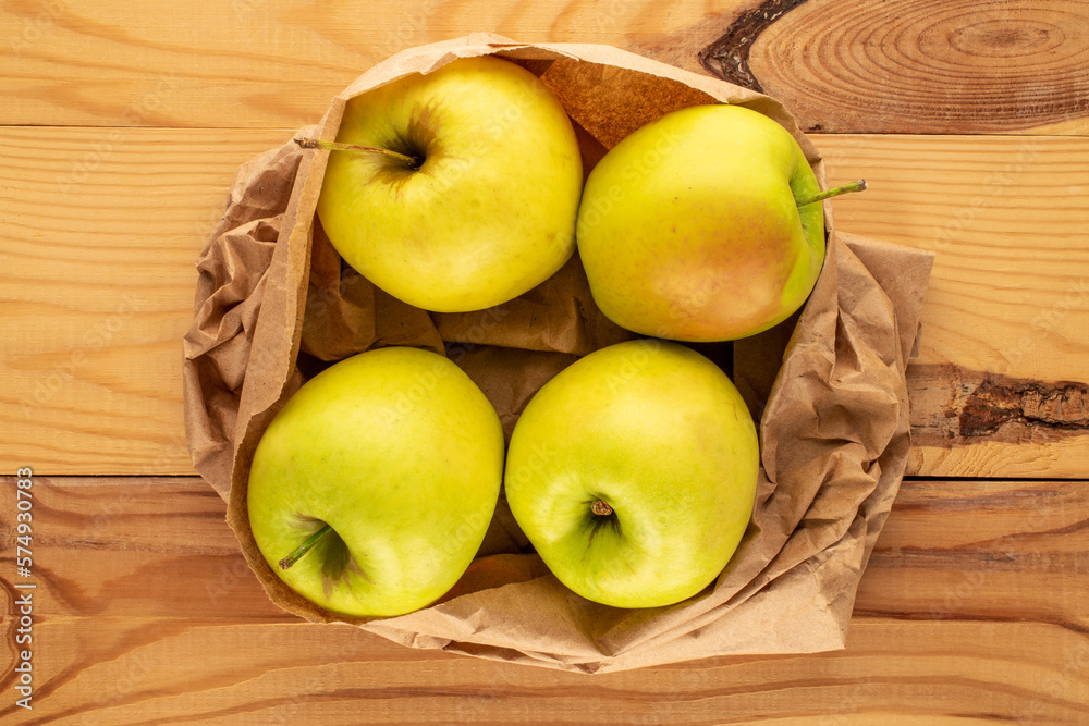 Four yellow organic apples in a paper bag on a wooden table, macro, top view. Four yellow organic apples in a paper bag on a wooden table, macro, top view.
