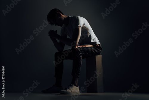 depressed and worried man feel the stigma about his depression and anxiousness caused by trauma, stress and social isolation while sit on wood block in the dark hands to head with bad mental health