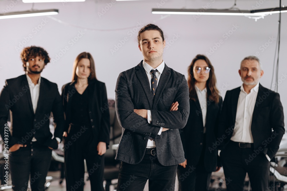 Young entrepreneur standing with arms crossed in front of his business partners. Business leadership, career growth. Front view of ceo and employees. Young entrepreneur standing with arms crossed in front of his business partners. Business leadership, career growth. Front view of ceo and employees.