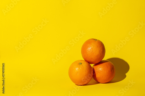 oranges fruits citrus ,three objects,hard shadow,orange color round,lie on the surface of the yellow background.concept juice vitamins.