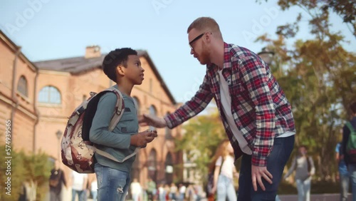 Young male teacher talk to African-American schoolboy outdoors. Realtime