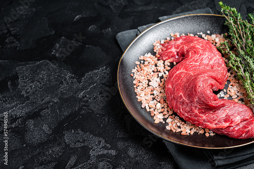 Raw Machete beef meat steak or hanging tender cut on plate with sea salt and thyme. Black background. Top view. Copy space