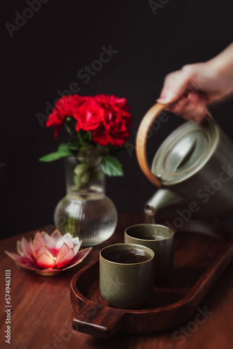 Hand pouring green tea in a Japanese style teapot and cups with dark background