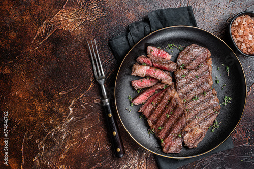 Barbecue denver strip beef meat steak on a plate. Dark background. Top view. Copy space