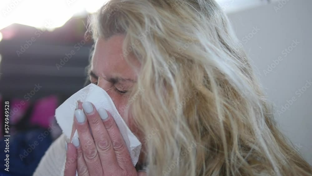 Close-up of a sick woman sneezing multiple times into a tissue.