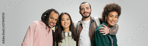 happy multicultural friends in trendy clothes smiling at camera isolated on grey, banner.