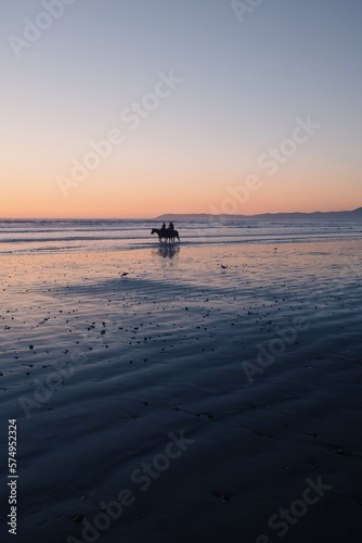 People riding horses on the beach at sunset in California