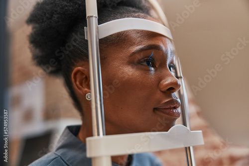 Laser, vision or black woman in eye exam for eyesight at optometrist or ophthalmologist consulting office. Face of optician helping a African customer testing or checking iris or retina visual health