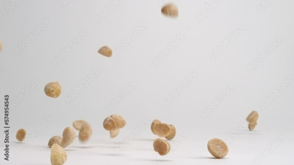 Shelled macadamia nut pieces falling onto white table top and bouncing into a pile in slow motion