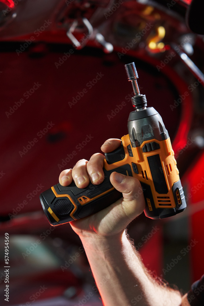 Fototapeta premium The hand of a caucasian man holds a cordless wrench against the background of a metal part