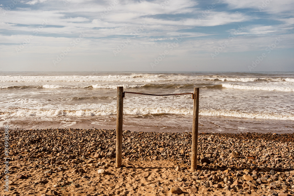 Sandy beach with wooden poles against wavy sea Sandy beach with wooden poles against wavy sea