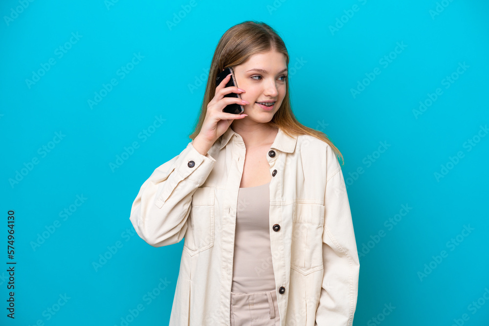 Teenager Russian girl isolated on blue background keeping a conversation with the mobile phone with someone Teenager Russian girl isolated on blue background keeping a conversation with the mobile phone with someone