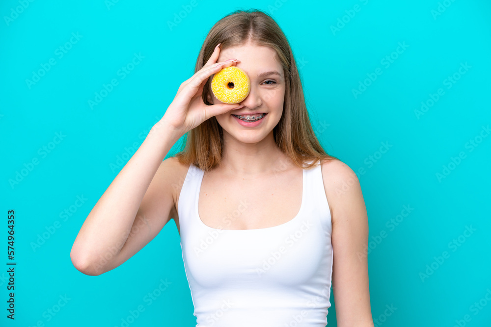 Teenager Russian girl isolated on blue background holding a donut and happy Teenager Russian girl isolated on blue background holding a donut and happy