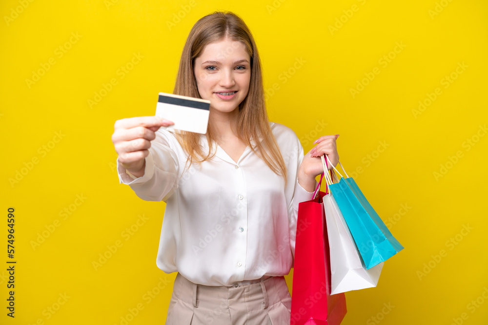 Teenager Russian girl isolated on yellow background holding shopping bags and a credit card Teenager Russian girl isolated on yellow background holding shopping bags and a credit card