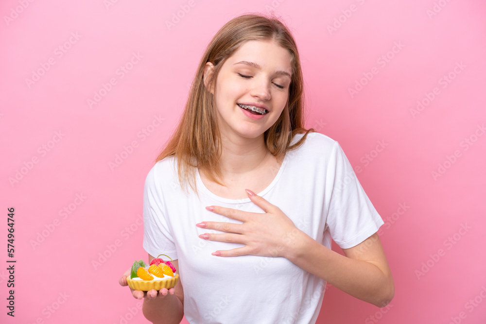 Teenager Russian girl holding a tartlet isolated on pink background smiling a lot Teenager Russian girl holding a tartlet isolated on pink background smiling a lot