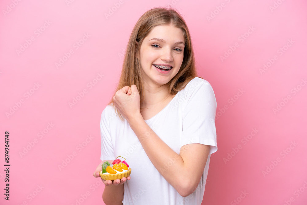 Teenager Russian girl holding a tartlet isolated on pink background celebrating a victory Teenager Russian girl holding a tartlet isolated on pink background celebrating a victory