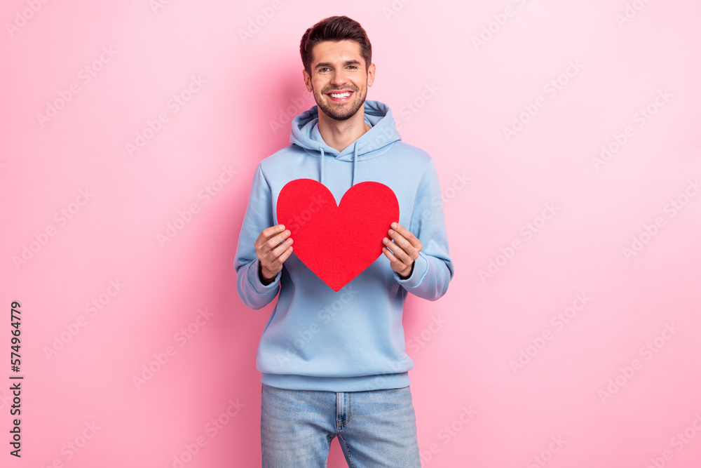 Photo of cheerful sweet guy dressed blue sweatshirt smiling holding red heart isolated pink color background Photo of cheerful sweet guy dressed blue sweatshirt smiling holding red heart isolated pink color background