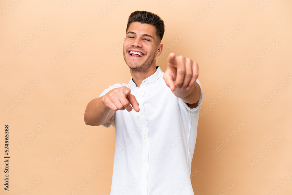 Young caucasian man isolated on beige background pointing front with happy expression Young caucasian man isolated on beige background pointing front with happy expression