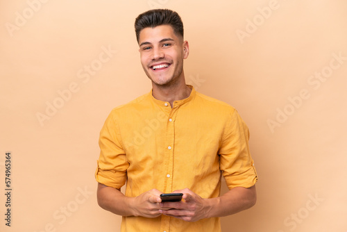 Young caucasian man isolated on beige background sending a message with the mobile © luismolinero