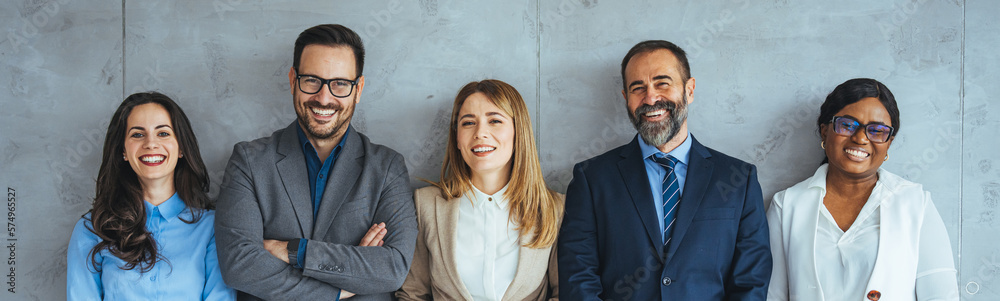 Multi-ethnic group of people in formal businesswear standing in a row. Group of business persons standing against a wall. Studio shot of a group of people waiting in a line against a gray background Multi-ethnic group of people in formal businesswear standing in a row. Group of business persons standing against a wall. Studio shot of a group of people waiting in a line against a gray background