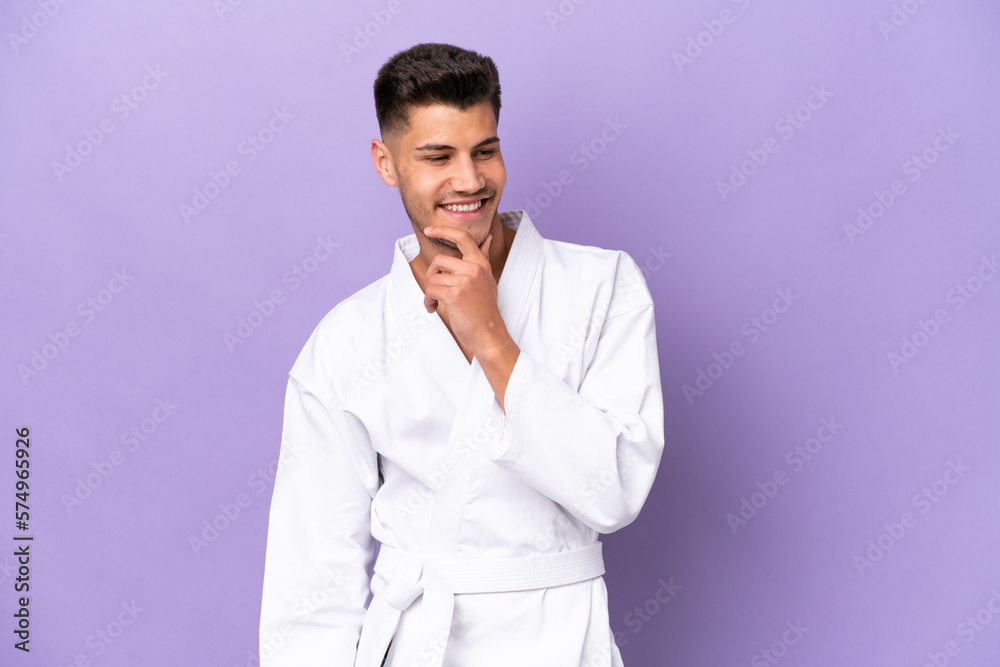 Young caucasian man doing karate isolated on purple background looking to the side and smiling Young caucasian man doing karate isolated on purple background looking to the side and smiling