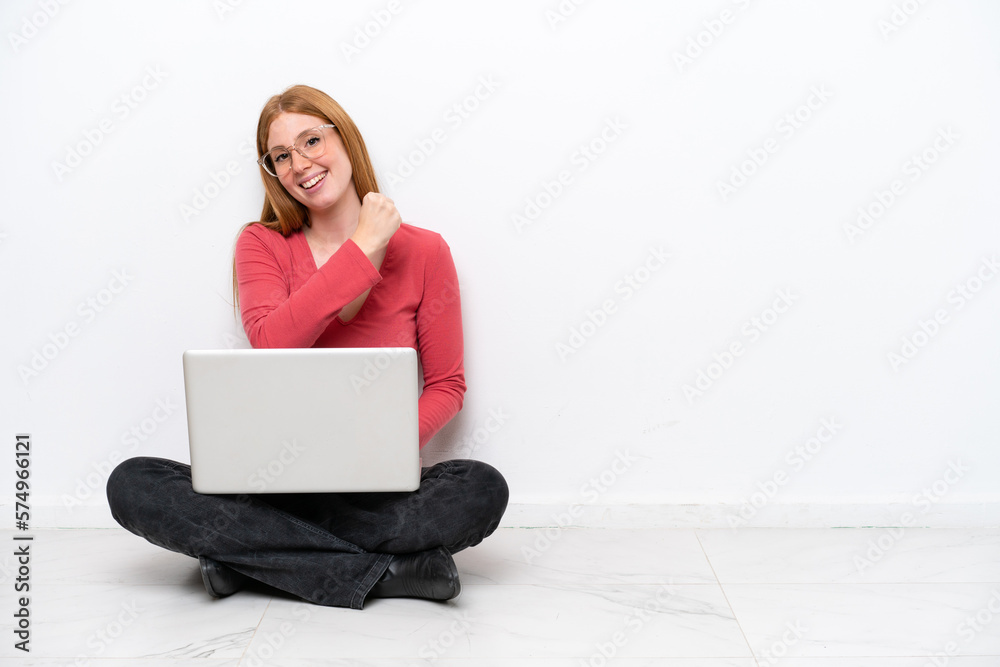 Young redhead woman with a laptop sitting on the floor isolated on white background celebrating a victory Young redhead woman with a laptop sitting on the floor isolated on white background celebrating a victory