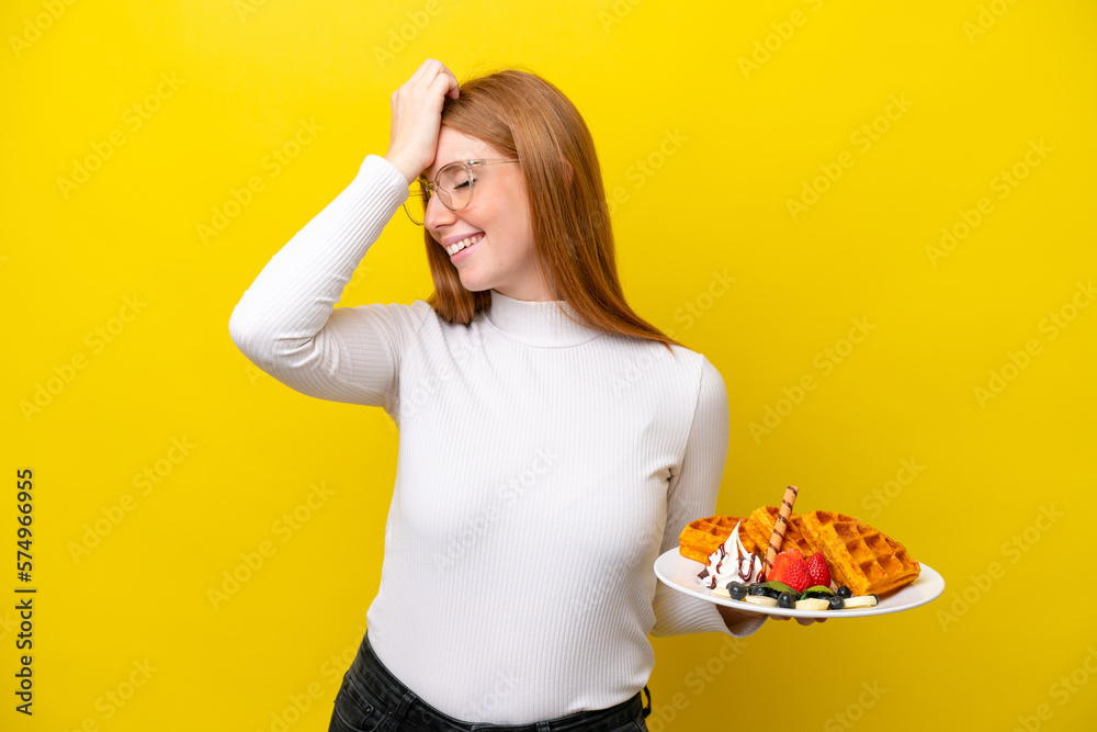 Young redhead woman holding waffles isolated on yellow background has realized something and intending the solution Young redhead woman holding waffles isolated on yellow background has realized something and intending the solution