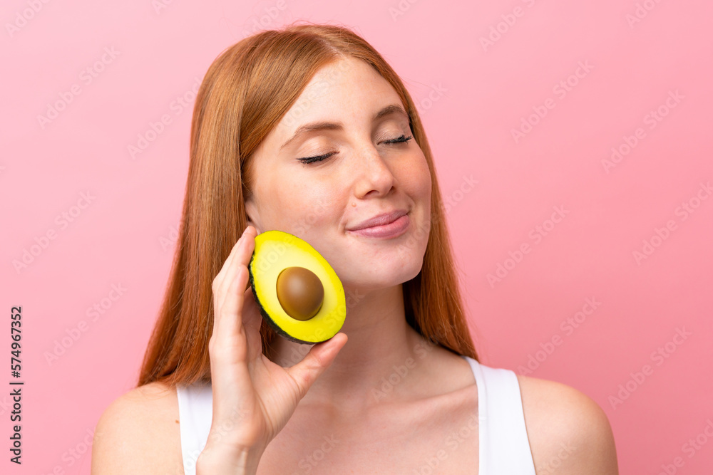 Young redhead woman isolated on pink background holding an avocado. Close up portrait Young redhead woman isolated on pink background holding an avocado. Close up portrait