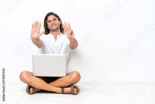 Young handsome man with a laptop sitting on the floor isolated on white background counting eight with fingers