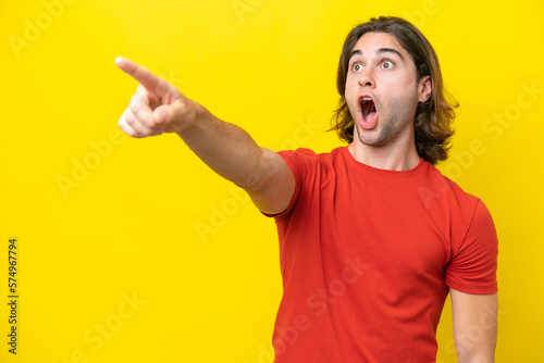 Caucasian handsome man isolated on yellow background pointing away