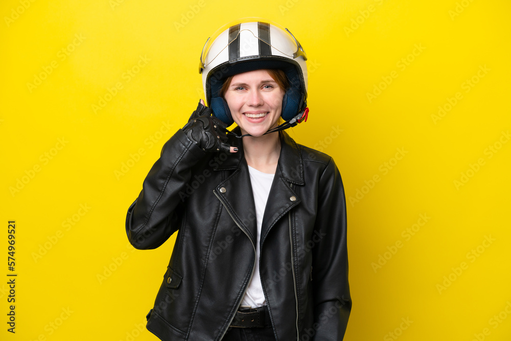 Young English woman with a motorcycle helmet isolated on yellow background making phone gesture. Call me back sign Young English woman with a motorcycle helmet isolated on yellow background making phone gesture. Call me back sign