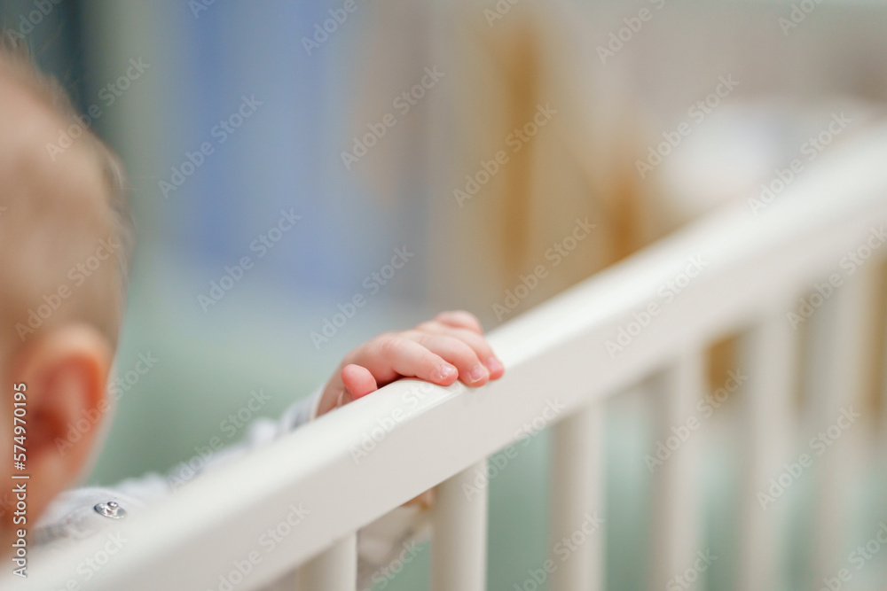 Baby's tiny hands in the crib holding onto the side of the bed. Closeup, baby development concept photo