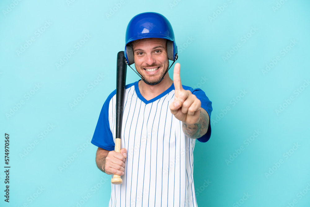 Baseball player with helmet and bat isolated on blue background showing and lifting a finger