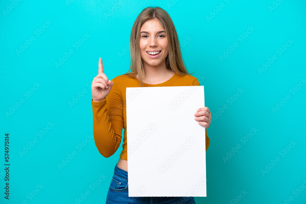 Young caucasian woman isolated on blue background holding an empty placard and pointing up Young caucasian woman isolated on blue background holding an empty placard and pointing up