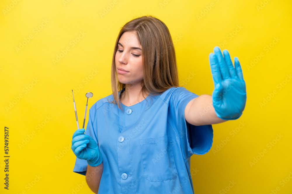 Dentist caucasian woman holding tools isolated on yellow background making stop gesture and disappointed Dentist caucasian woman holding tools isolated on yellow background making stop gesture and disappointed