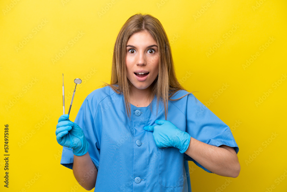 Dentist caucasian woman holding tools isolated on yellow background with surprise facial expression Dentist caucasian woman holding tools isolated on yellow background with surprise facial expression
