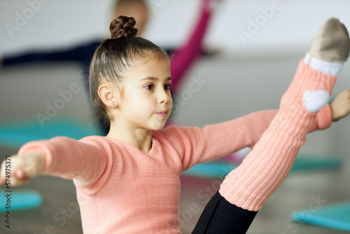 Little beautiful girl, child training, doing stretching exercises indoors. Gracefulness and flexibility. Unfocused background. Concept of sportive lifestyle, childhood, education, professional sport