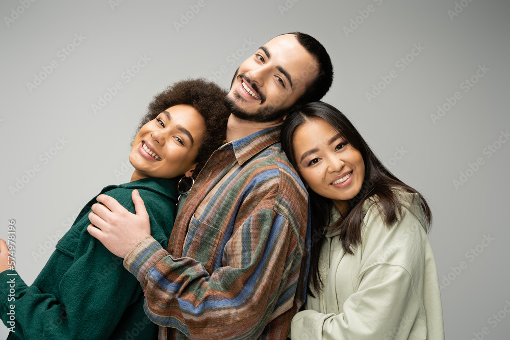 joyful multicultural friends in trendy outfit smiling at camera while posing isolated on grey. joyful multicultural friends in trendy outfit smiling at camera while posing isolated on grey.