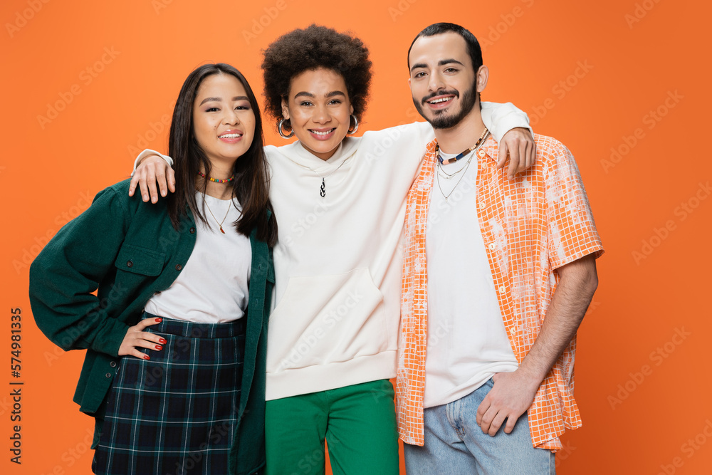 cheerful african american woman embracing trendy multiracial friends isolated on orange. cheerful african american woman embracing trendy multiracial friends isolated on orange.