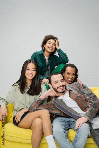 happy african american woman looking away near multiethnic friends sitting on yellow sofa isolated on grey.