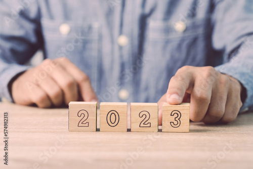 Businessman's hand is sorting out a wooden dice with the number of 2023 on the table. Work concept in 2023