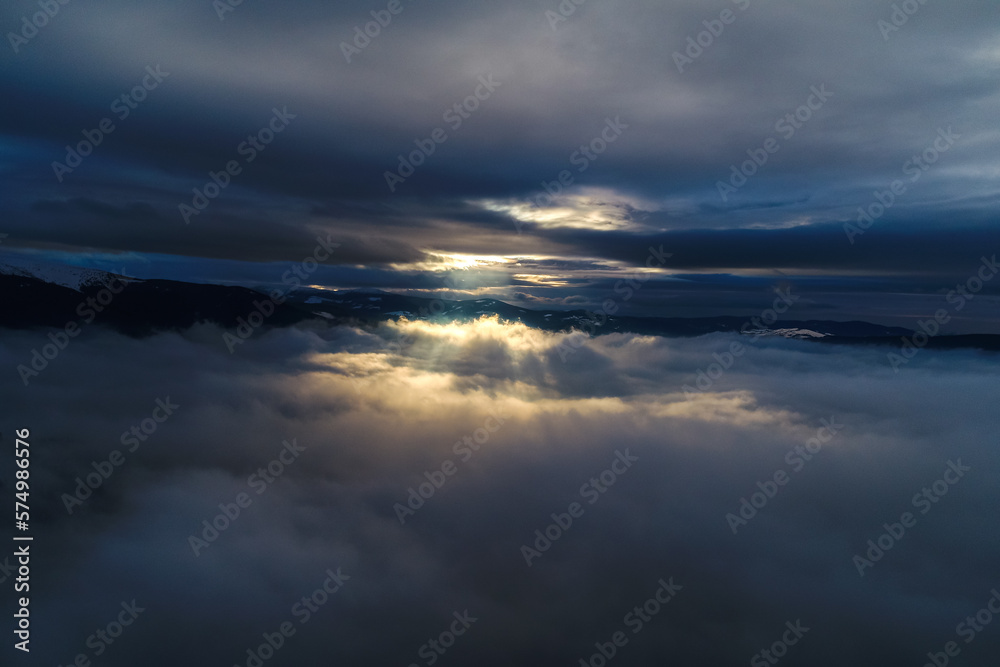 Dramatic winter sunset between the clouds. Aerial view on top of the clouds during with sun rays bursting out of the sky.