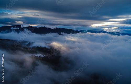 Dramatic winter sunset between the clouds. Aerial view on top of the clouds during with sun rays bursting out of the sky. © Dragoș Asaftei