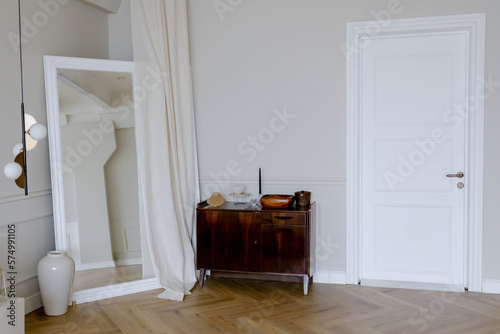 Stylish chest of drawers next to the white front door in the room. Large mirror in the corner.