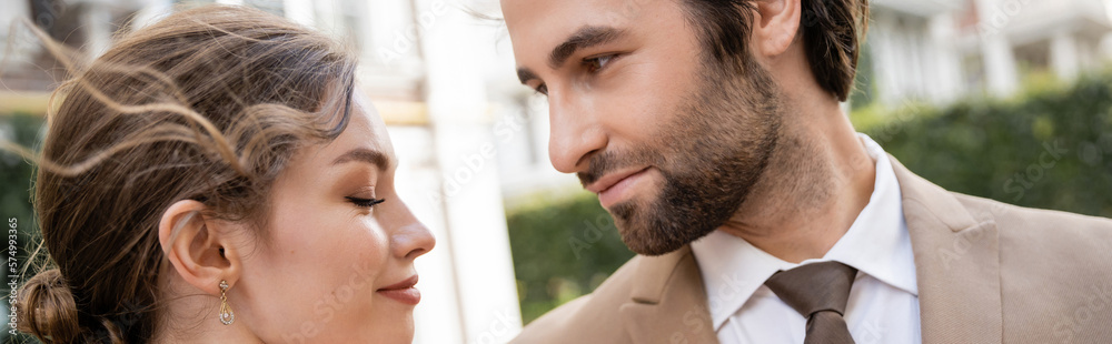 Obraz premium bearded man in suit looking at smiling bride outdoors, banner.