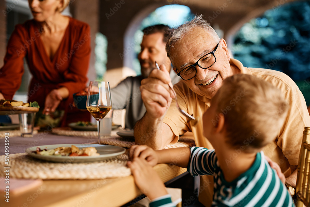 Happy senior man feeding his grandson during family meal at dining table.