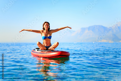 beautiful woman practising yoga on paddle sup surfboard