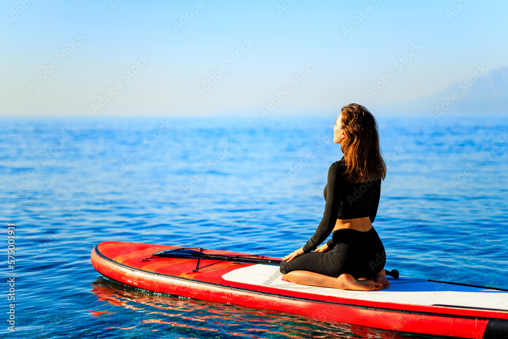 Obraz premium beautiful woman practising yoga on paddle sup surfboard